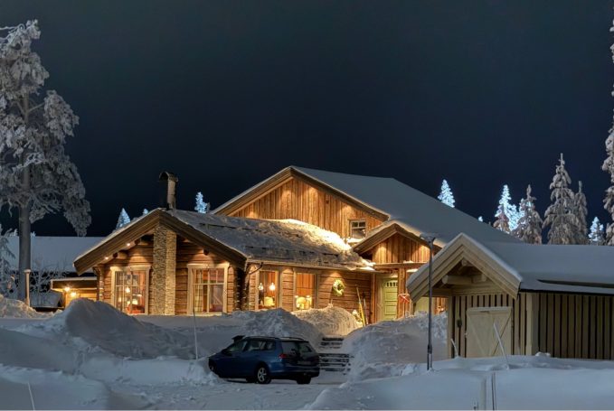 Stuga i snö med belyst utsida och en bil parkerad framför.